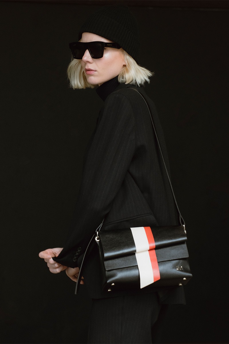 Drapé_Graphic_black_modelo Mujer posando con Bolso de piel negro con banda vertical blanca y roja marca HedenBrand, colección Drape Graphic terracota