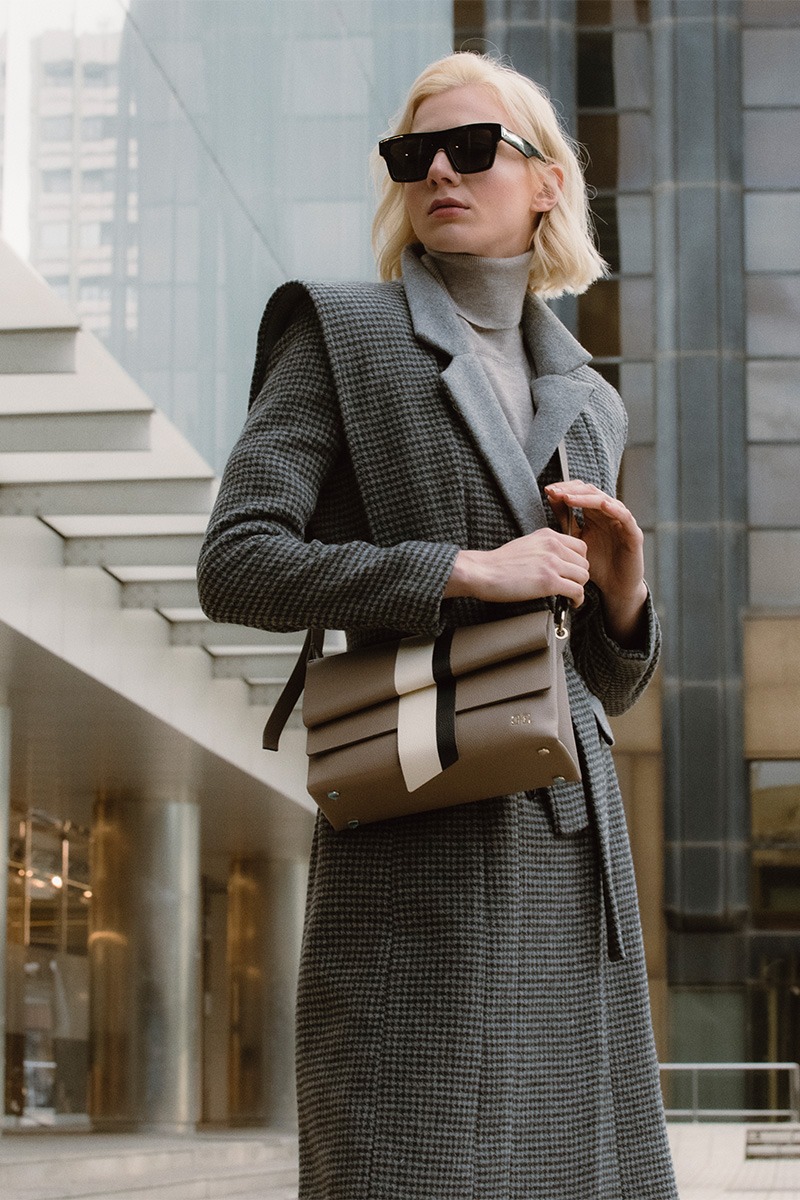 Mujer posando con Bolso de piel marrón con banda vertical blanca y negra marca HedenBrand, colección Drape Graphic terracota