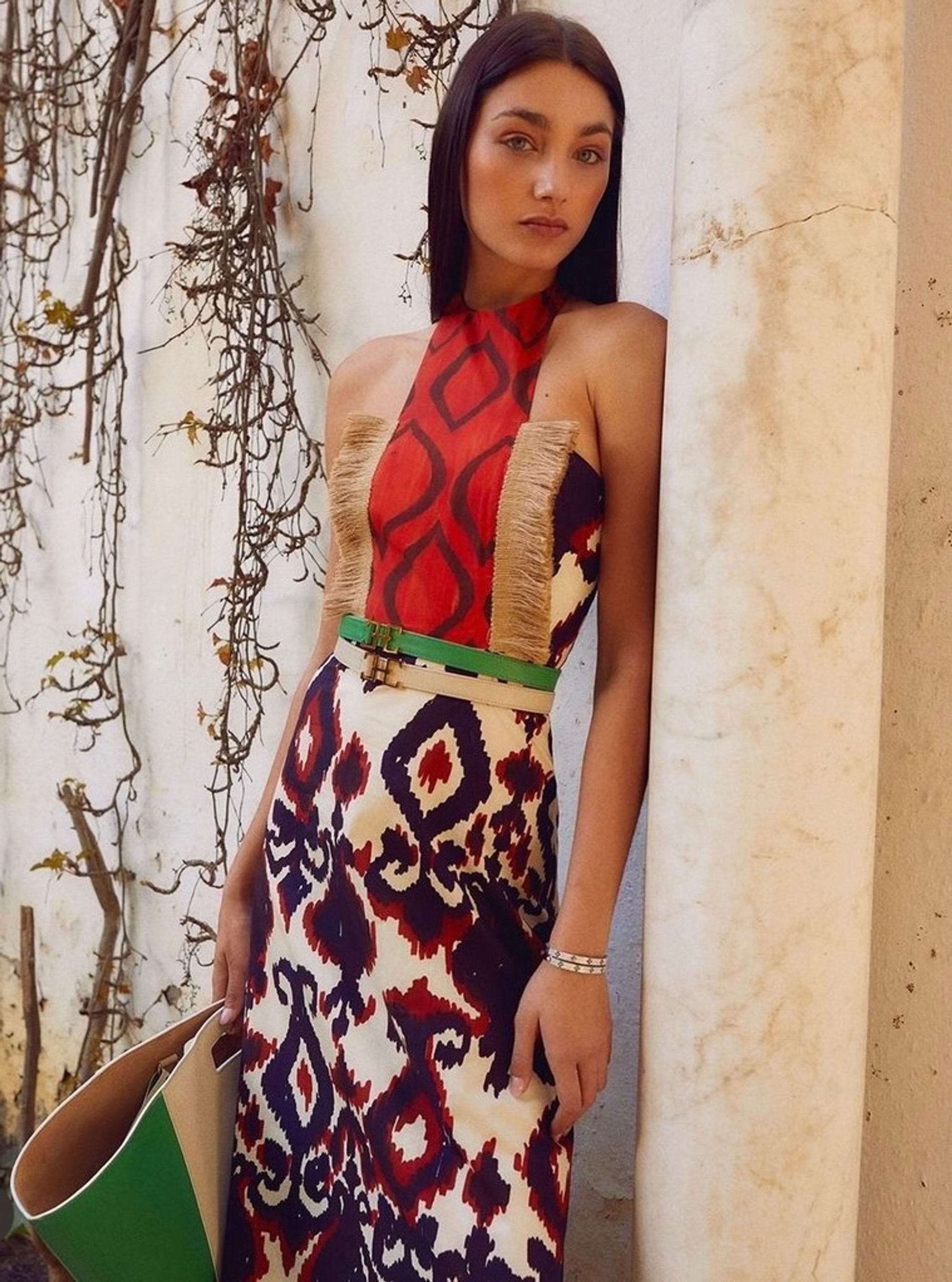 Mujer posando con bolso y cinturón de piel marca hedenBrand, con una casa y ramas de fondo